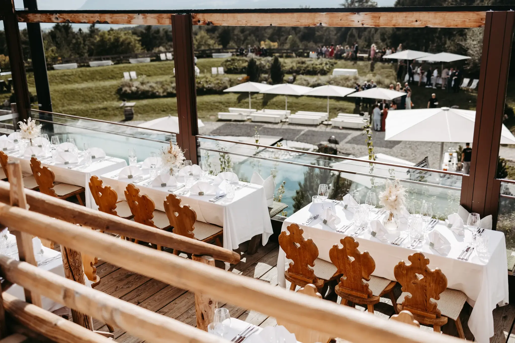 Hochzeitstische mit Tiroler Holzstühlen auf der Terrasse der Stöttlalm mit Blick auf Badeteich und Berge