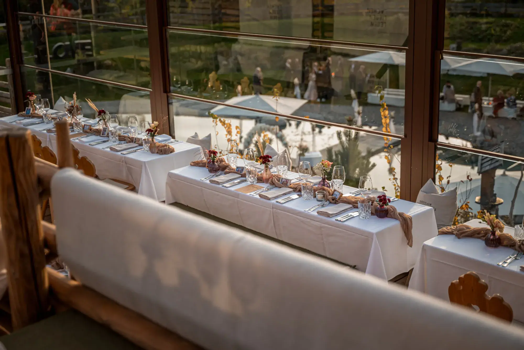 Weiss gedeckte Festtafeln mit Herbstdeko an den Panoramafenstern der Stöttlalm mit Gartenblick