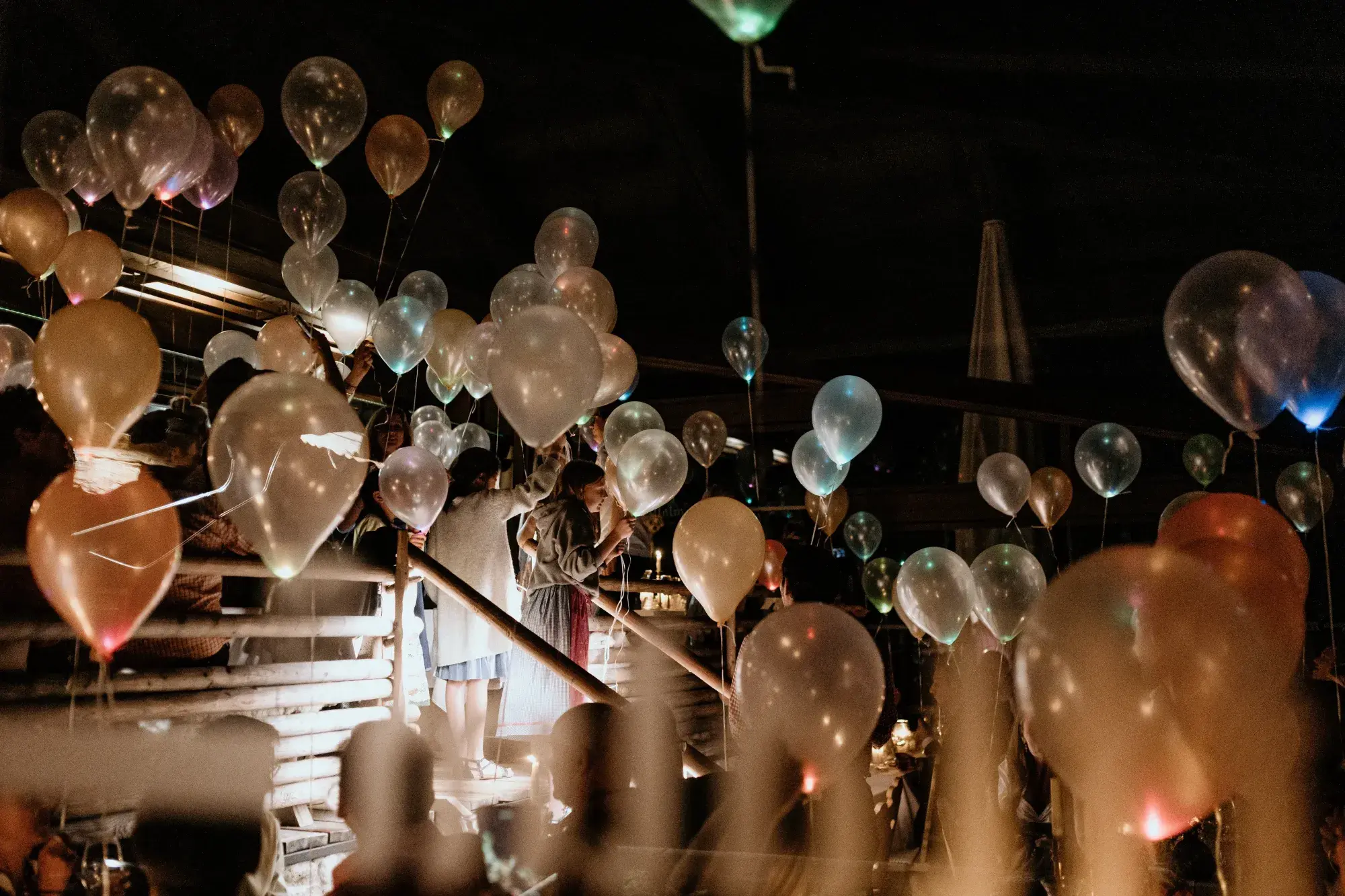 Gäste mit leuchtenden Ballons auf der Holztreppe der Stöttlalm bei einer Abendfeier