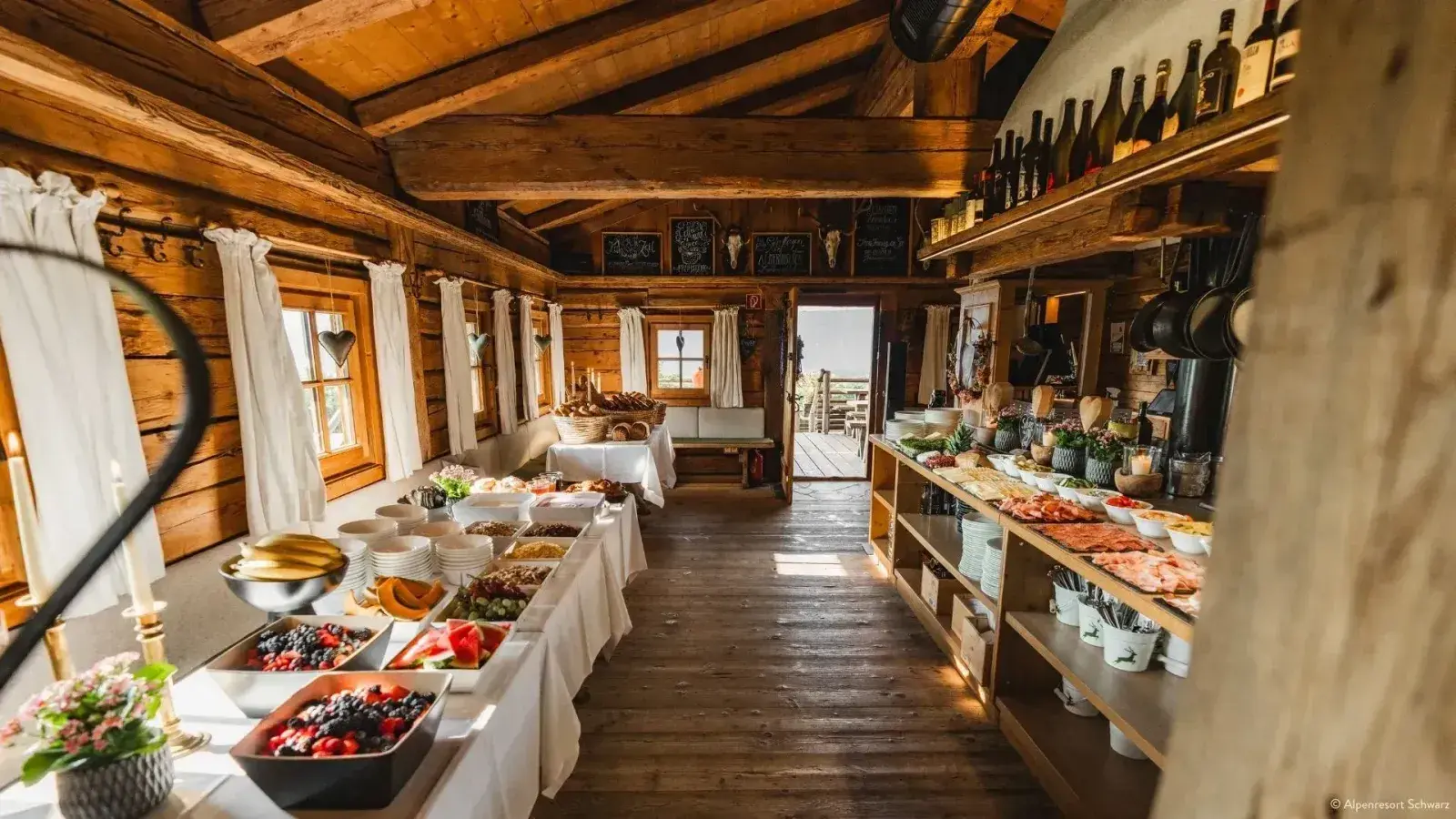 Hüttenbrunch-Buffet in der holzvertäfelten Almstube der Stöttlalm mit offener Tür und Bergblick